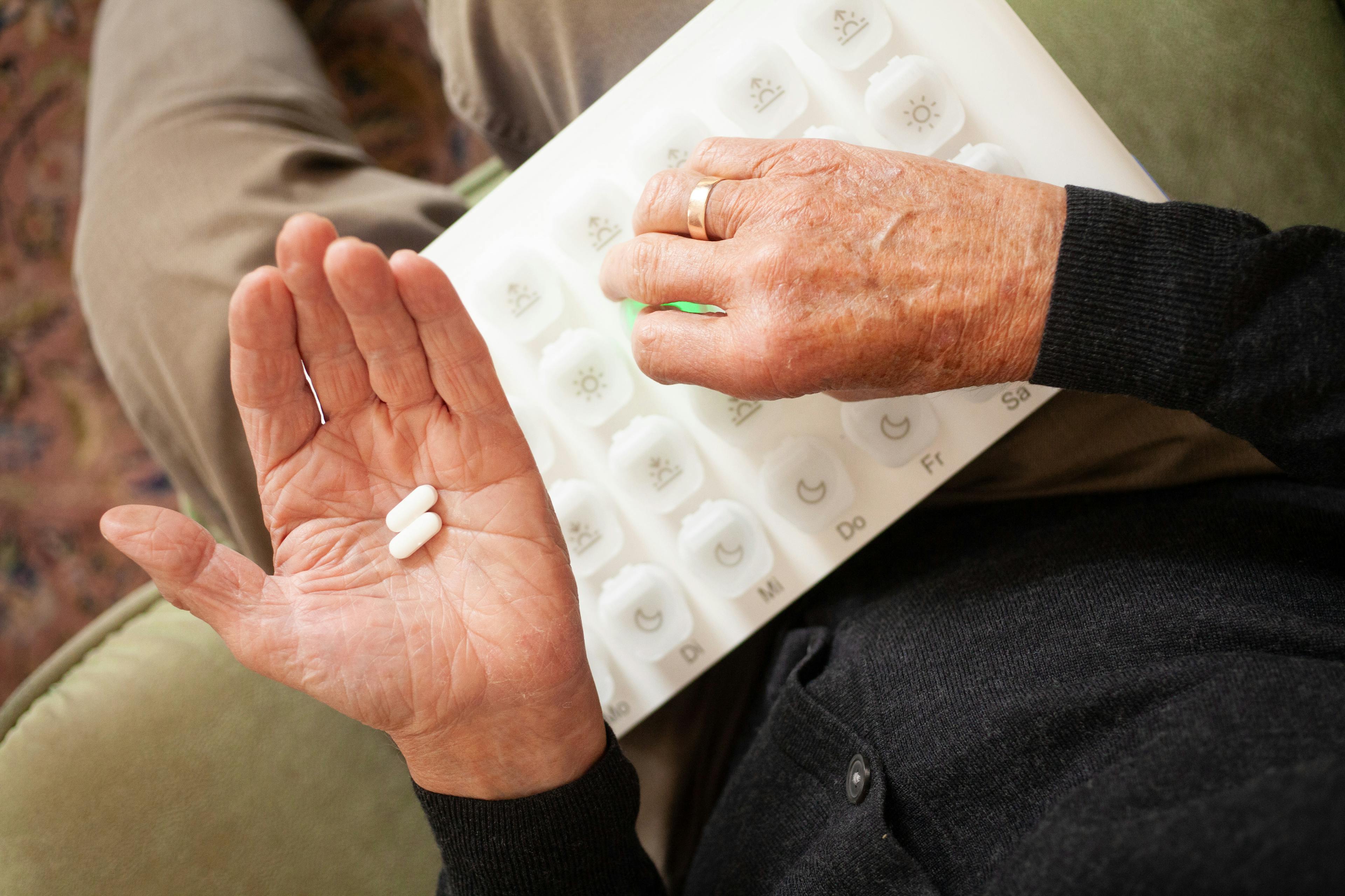 Medikamente in Hand mit Medikamentenspender von oben fotografiert